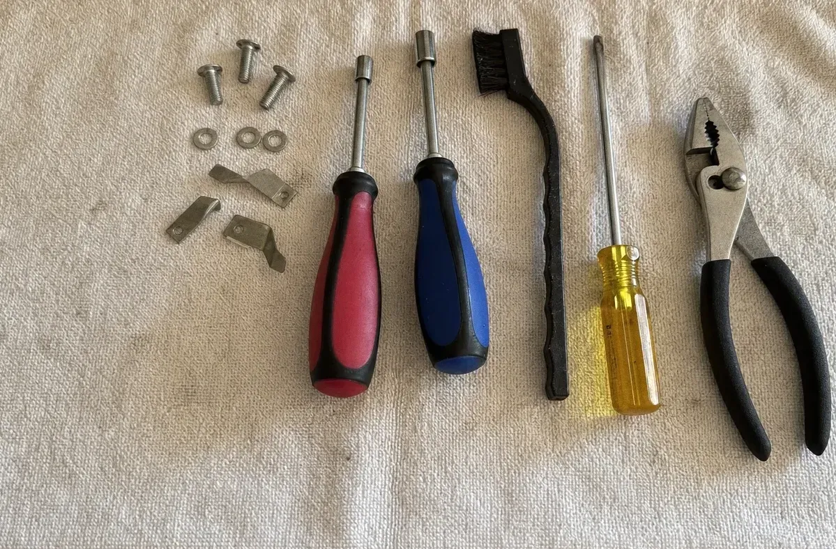 Red and blue handled screwdrivers, a yellow nut driver, a wire brush and pliers laid on a white towel with small clips